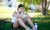 A teenage girl sits on the grass in a park to check the display on her fitness tracker