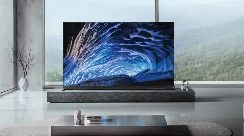 A Toshiba TV with a beautiful ice cave on the screen in a modern grey living room overlooking a forest