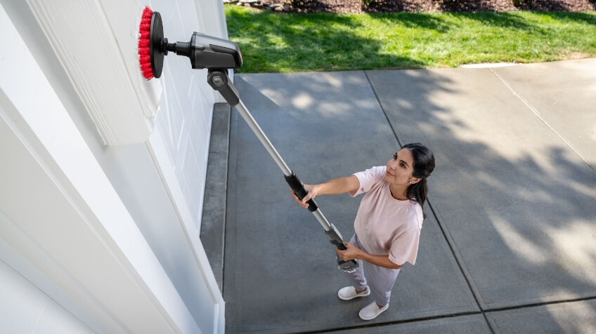 woman cleans shed wall with Hoover 18V ONEPWR Telescopic Scrubber