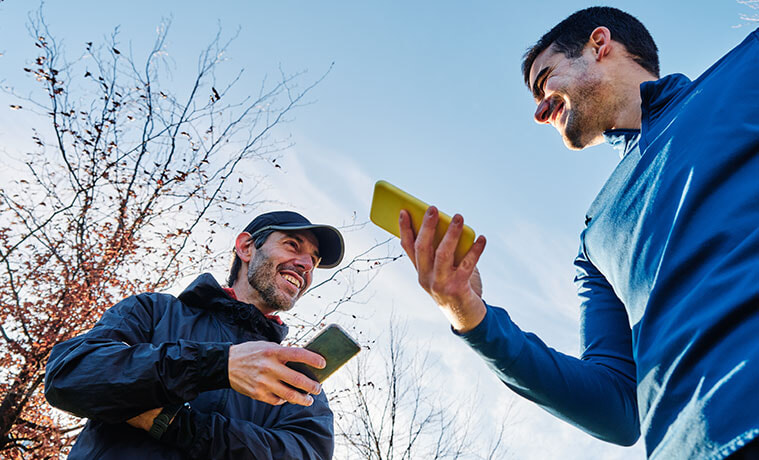 Two men out having a walk in the sunshine stop to compare smartphones