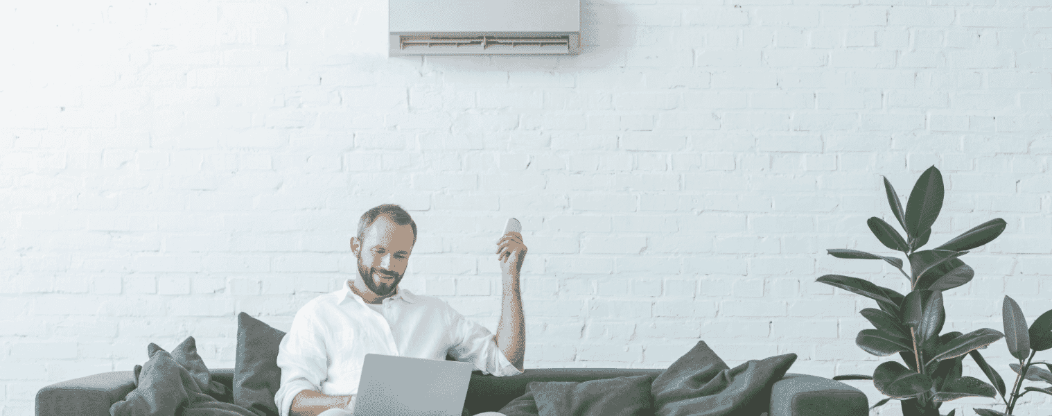 Man relaxes on his computer as he changes the temperature on his air conditioner