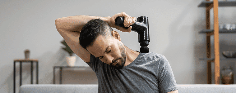 A man uses a massage gun to relieve tension in his shoulder