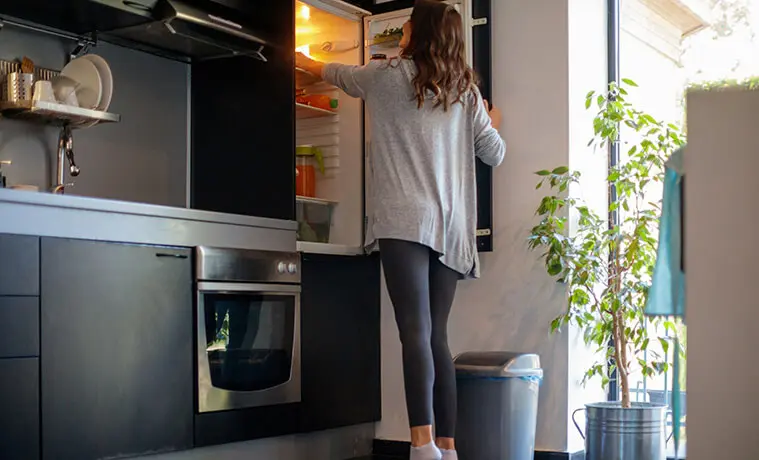 Woman reaches into her fridge to fetch food from the upper shelf