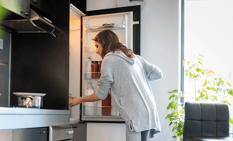 Woman opens a bottom mount fridge to remove ingredients for her lunch