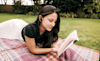 Woman relaxing in a park whilst reading and using her new Noise Cancelling Headphones