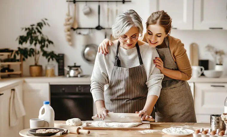 A mother and her adult daughter bake together in the kitchen.