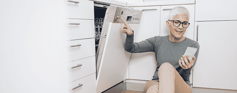 A woman sits on the floor near her WiFiconnected dishwasher to link it to her smartphone