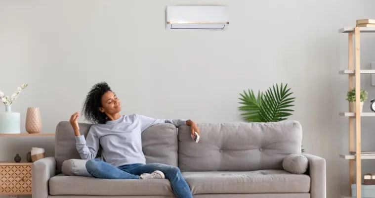 A woman relaxes in her living room while her split system air conditioner keeps the room cool