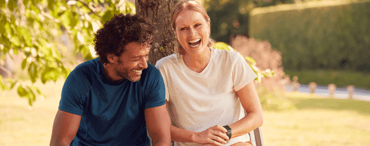 A man and woman sit on a bench outdoors with fitness trackers on their wrists