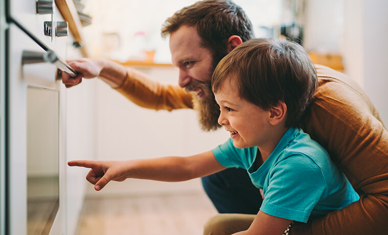 A father and his young son look through the oven door to see if dinner is ready