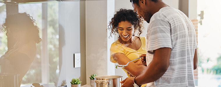 A young couple cooks together in their kitchen watching a steaming pot sitting on a gas cooktop 