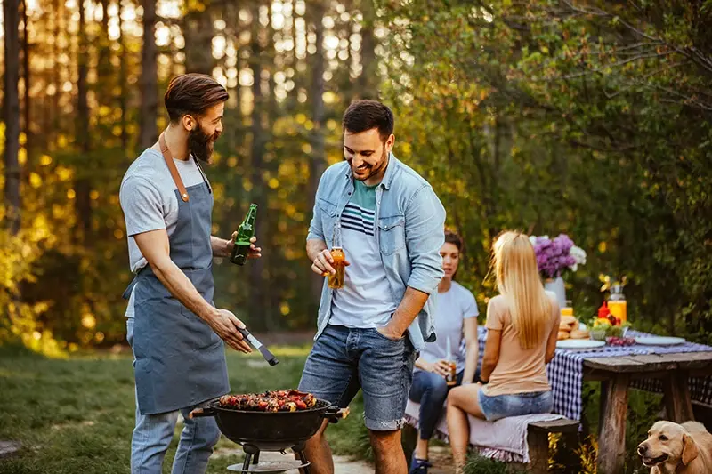 Two men standing and talking next to a small charcoal BBQ