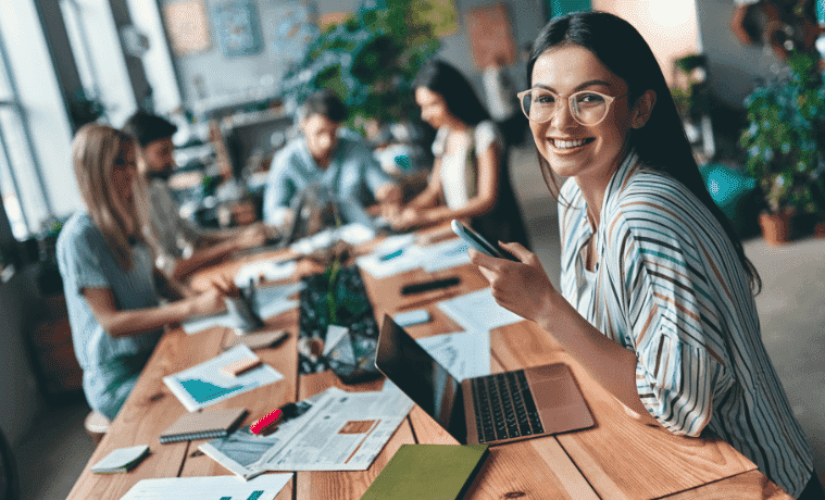 A female student works on her laptop at a communal table with other students