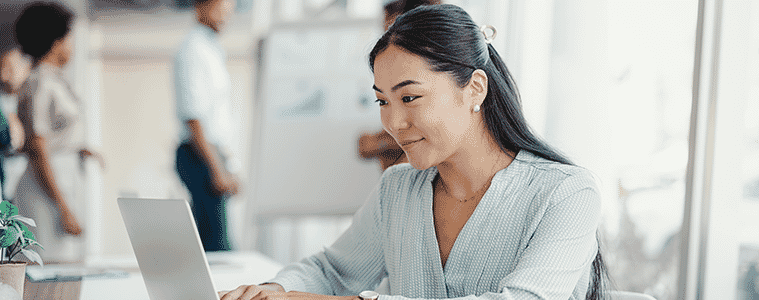 Female executive busy working on a laptop  with colleagues in the background