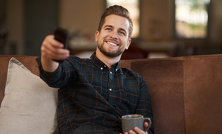 Man changes channels on wallmounted big screen TV using a remote control
