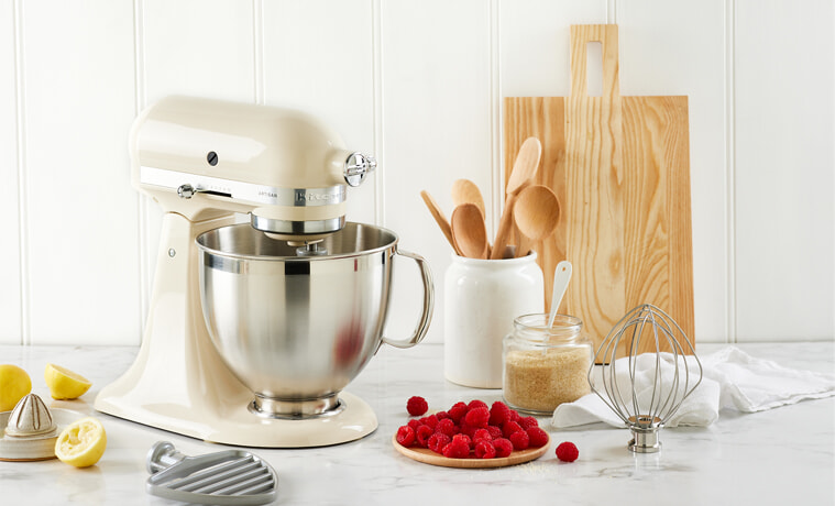 A cream coloured KitchenAid Artisan Stand Mixer sits in a white modern kitchen on a grey benchtop
