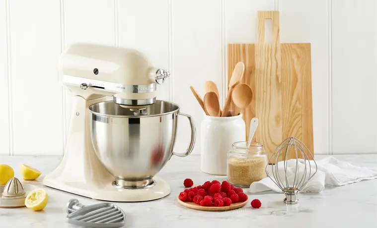 A cream coloured KitchenAid Artisan Stand Mixer sits in a white modern kitchen on a grey benchtop