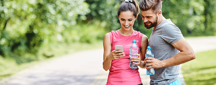 A man and woman take a break on their run and look at an app on their smartphone