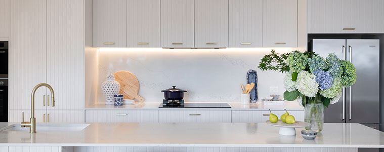 White Hamptonsstyle kitchen with VJ cabinetry stainless steel french door fridge gold gooseneck tap and white wicker kitchen stools
