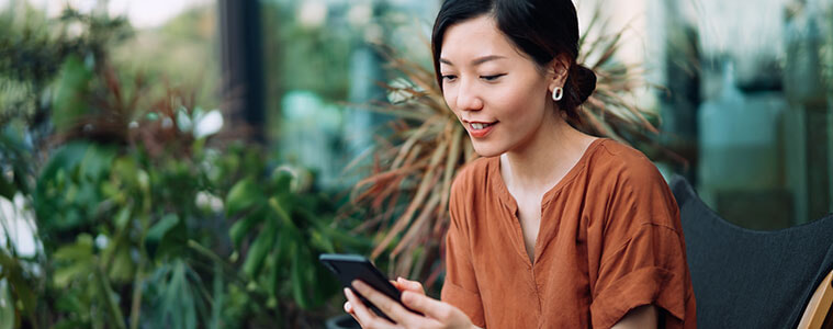 Young woman sitting in a deck chair in her courtyard using her mobile phone