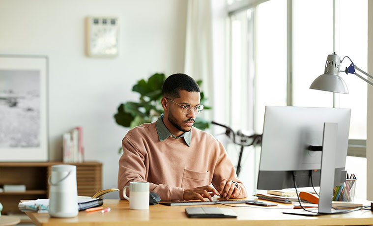 A man sits at the desk in his home office to type notes into his personal computer