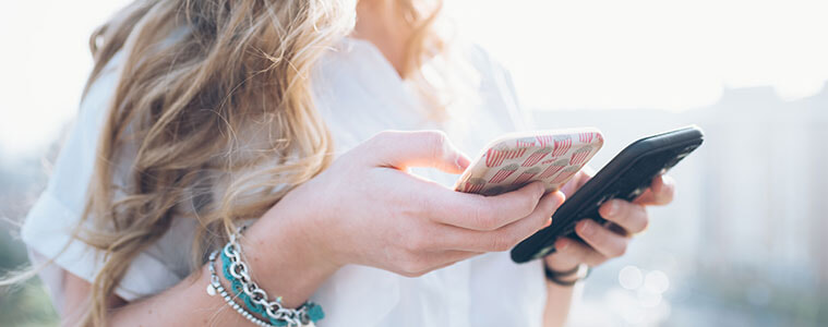 Young fashionable woman holds different sized smartphones in either hand weighing up the options