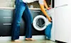 Waistdown view of a man in blue jeans loading white bed linen into a front loader washing machine