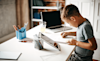 A primary school aged child does his homework while sitting at a desk with a tablet and laptop computer