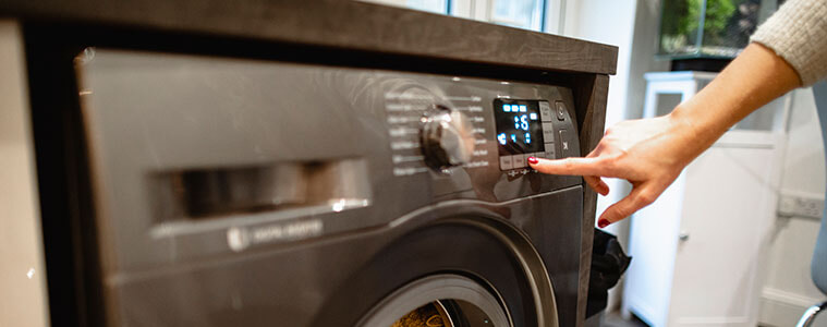 Close up of a hand pushing a button on a stainless steel laundry appliance