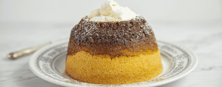 An individual treacle pudding all buttery sponge cake and sticky golden syrup served on a plate with a dollop of cream
