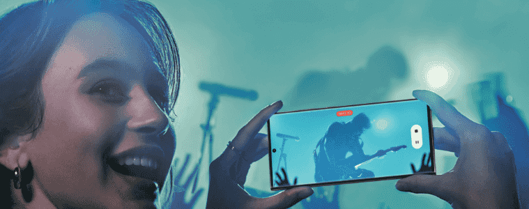 Smiling woman taking a video at a concert using her new Samsung Galaxy S23 mobile phone