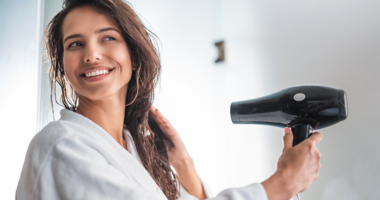 Woman smiling while using hair dryer.