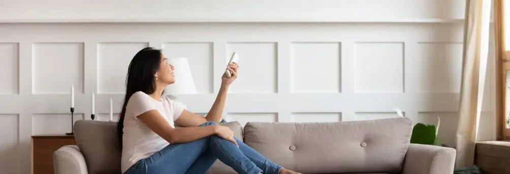 A woman siting on couch holding a aircon remote controller