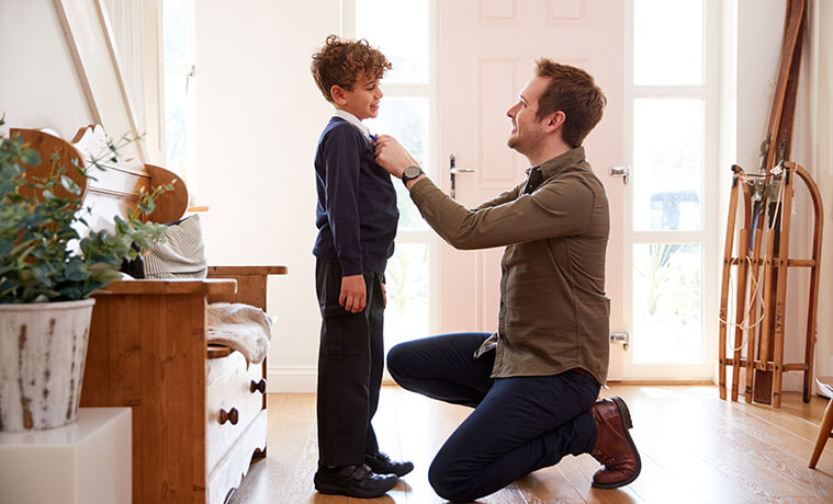 Kneeling man straightens his sons school uniform collar