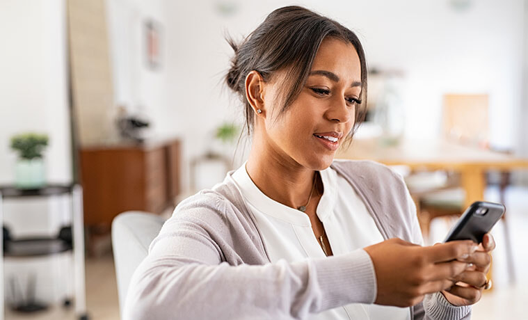 Woman uses her smartphone while relaxing on the couch at home