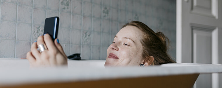 A woman relaxes in the bath while making some online purchases on her smartphone