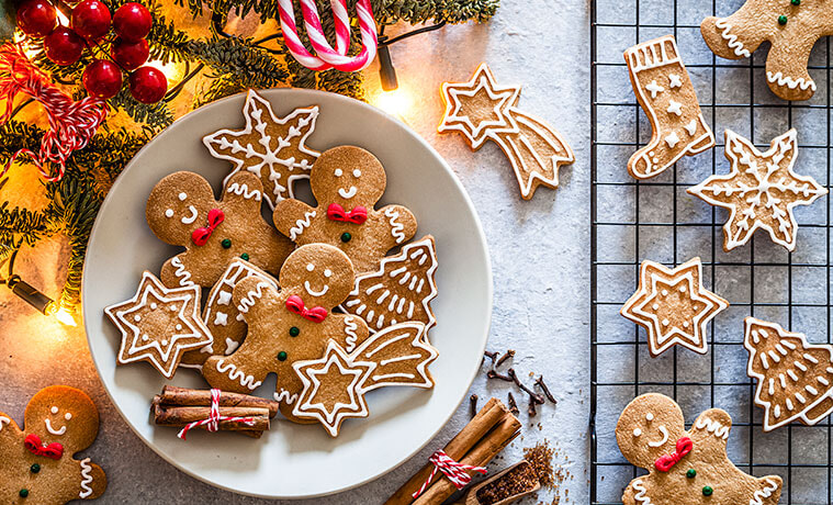 Gingerbread men and gingerbread snowflake cookies on a white plate and cooling rack with holly and berries