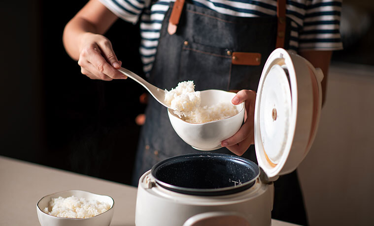 Woman scooping fluffy cooked rice from a benchtop rice cooker