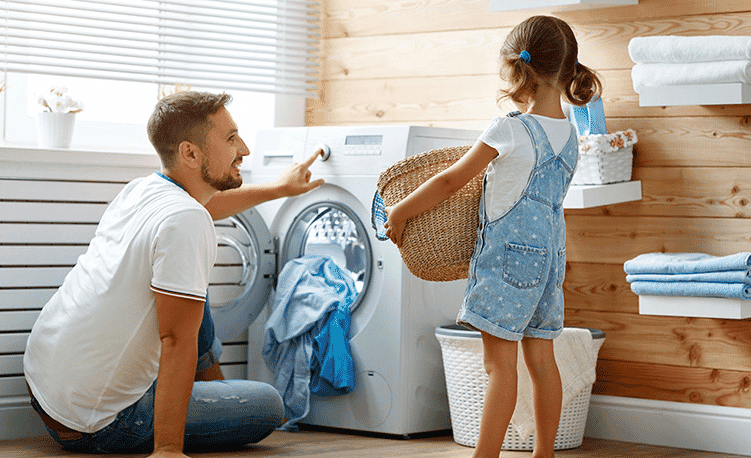 A father and daughter place a load of washing into a front loading washing machine in their laundry