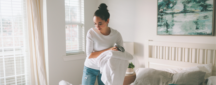 Woman in a white bedroom cleaning her bed