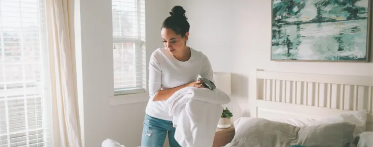 Woman in a white bedroom cleaning her bed