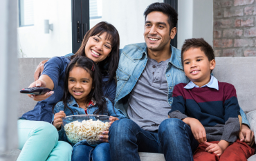 Father and his kids watching a movie on the couch with popcorn