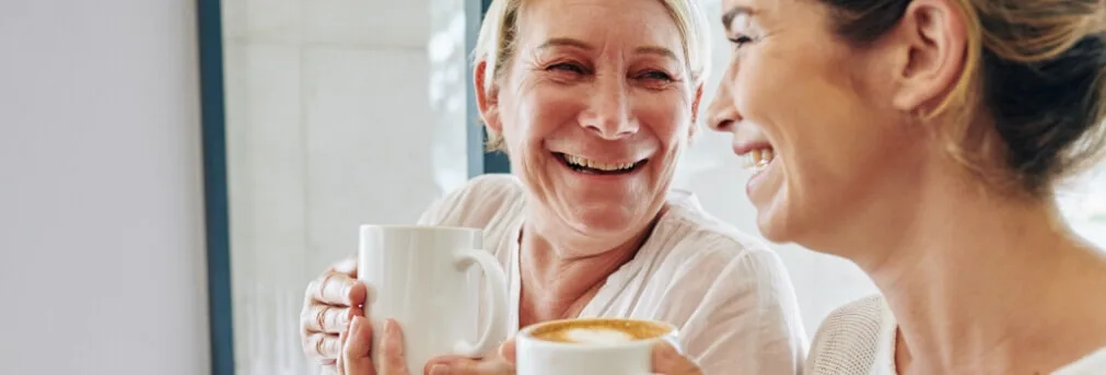 Two women laughing and enjoying a cup of coffee
