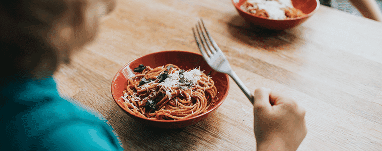 A young boy holds his fork above a bowl of homemade spaghetti in a red bowl