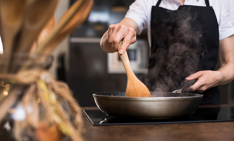 Closeup of a woman in a black apron using a pan on her induction cooktop at home