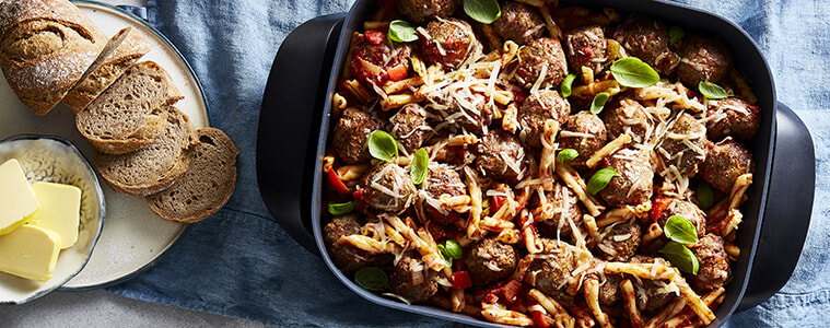 Meatballs garnished with basil and cheese sit in a benchtop frypan on a bench