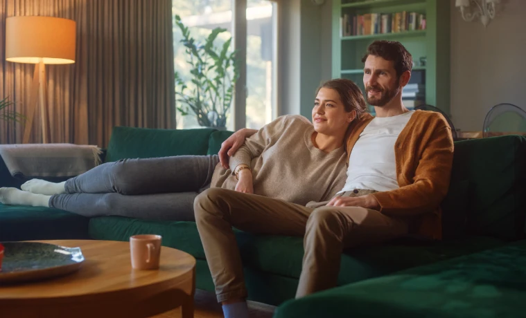 Couple sit to watch TV at home on green