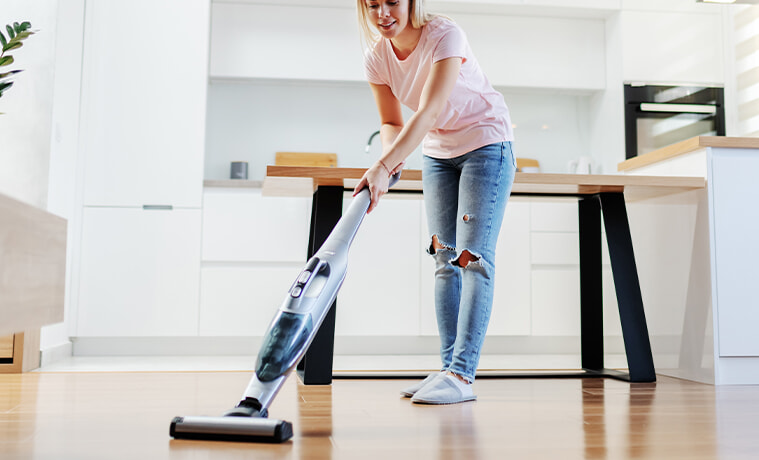 Woman using stick vacuum to clean her modern kitchen 