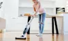Woman using stick vacuum to clean her modern kitchen 