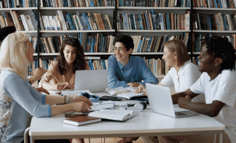 uni students sitting together in class doing work on their laptops and tablets 